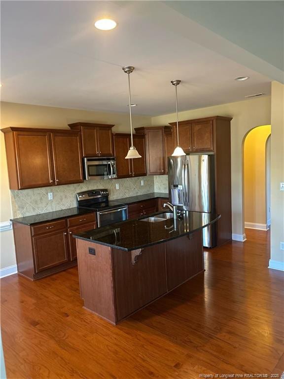 kitchen featuring dark wood-type flooring, arched walkways, stainless steel appliances, and a sink