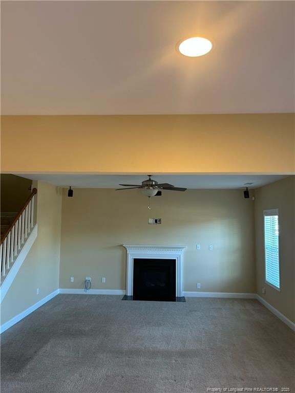 unfurnished living room with a ceiling fan, a fireplace with flush hearth, baseboards, and carpet flooring