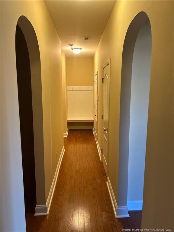 corridor with arched walkways, baseboards, and wood finished floors