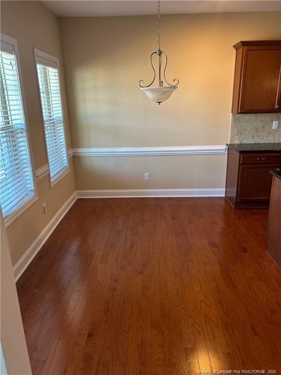 unfurnished dining area with dark wood finished floors and baseboards