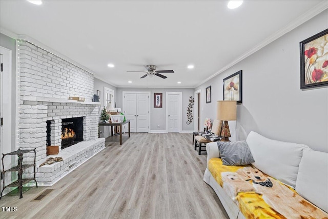 living room featuring a brick fireplace, ceiling fan, light hardwood / wood-style floors, and ornamental molding