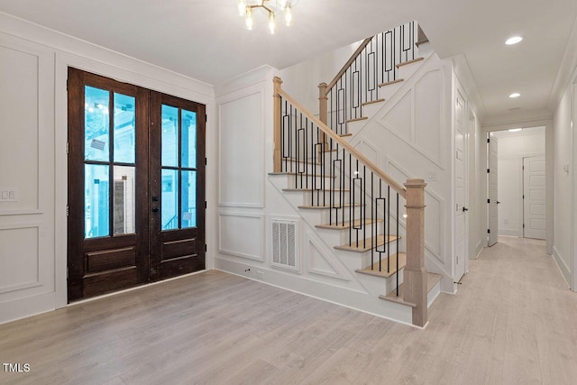 entryway with light hardwood / wood-style flooring, french doors, and an inviting chandelier