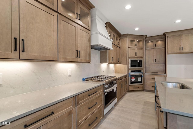 kitchen with backsplash, light hardwood / wood-style flooring, light stone countertops, stainless steel appliances, and custom range hood