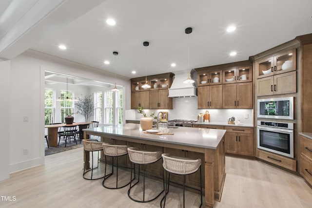 kitchen featuring stainless steel appliances, premium range hood, light wood-style floors, a breakfast bar, and recessed lighting