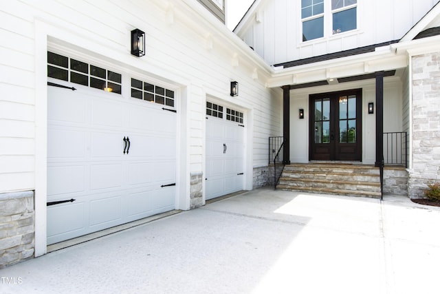 doorway to property featuring french doors, board and batten siding, stone siding, a garage, and concrete driveway