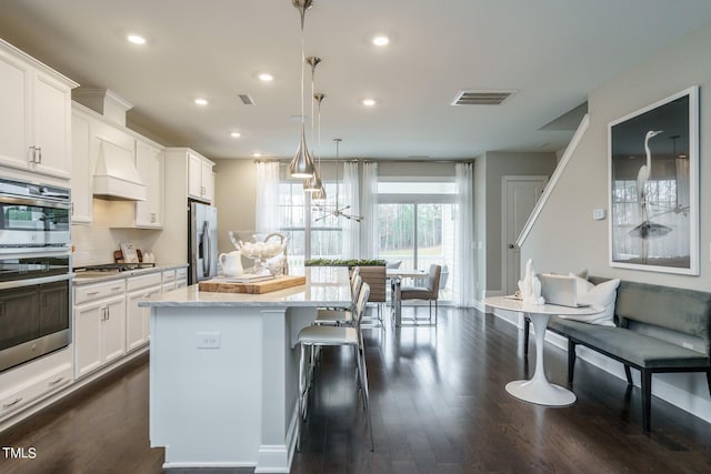 kitchen featuring white cabinets, decorative light fixtures, premium range hood, and appliances with stainless steel finishes