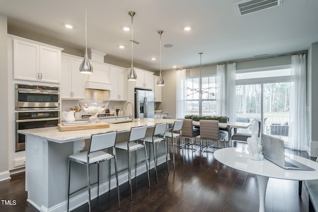 kitchen with pendant lighting, a center island with sink, dark hardwood / wood-style floors, appliances with stainless steel finishes, and white cabinetry