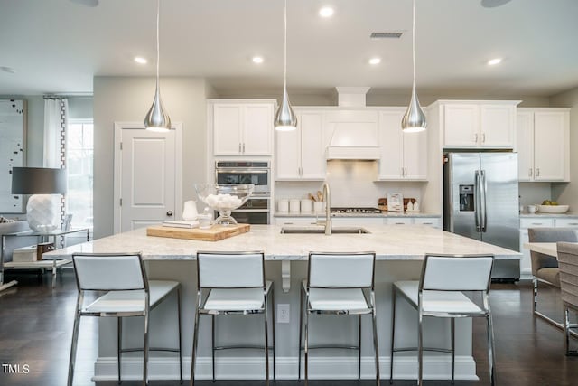 kitchen with pendant lighting, custom exhaust hood, sink, white cabinetry, and stainless steel appliances