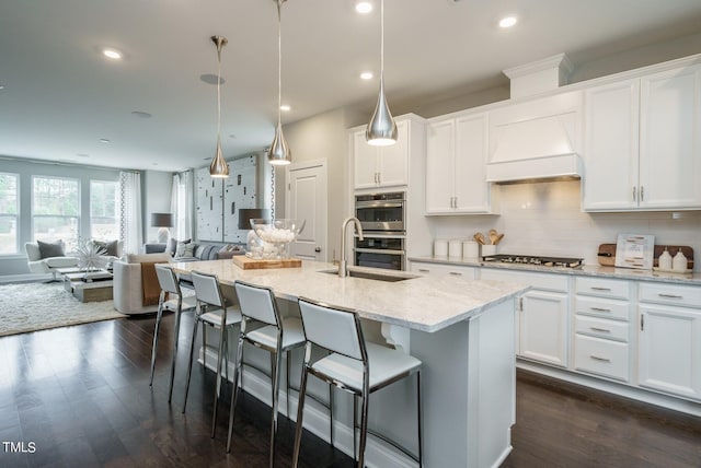 kitchen featuring an island with sink, white cabinets, dark wood-type flooring, and decorative light fixtures