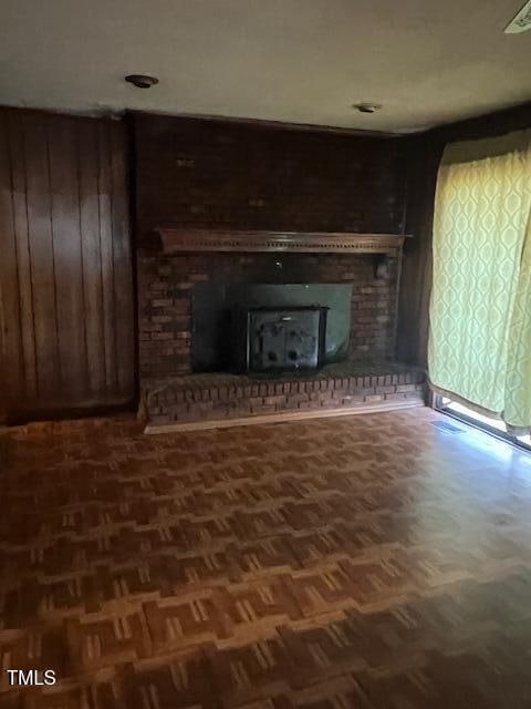 unfurnished living room featuring parquet flooring, a wood stove, and wooden walls