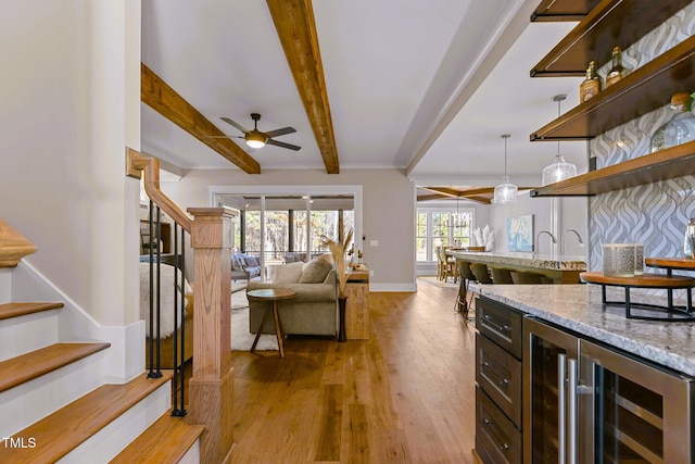 kitchen with hanging light fixtures, ceiling fan, beamed ceiling, light stone counters, and beverage cooler