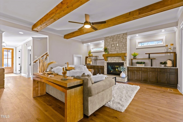 living room featuring ceiling fan, crown molding, beam ceiling, a fireplace, and light hardwood / wood-style floors