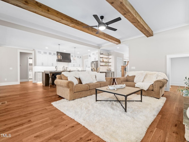 living room featuring beamed ceiling, light hardwood / wood-style flooring, ceiling fan, and crown molding