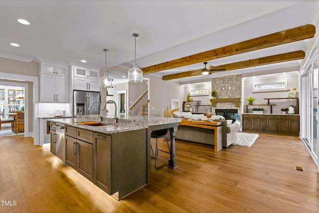 kitchen featuring appliances with stainless steel finishes, decorative light fixtures, white cabinetry, and a kitchen island with sink