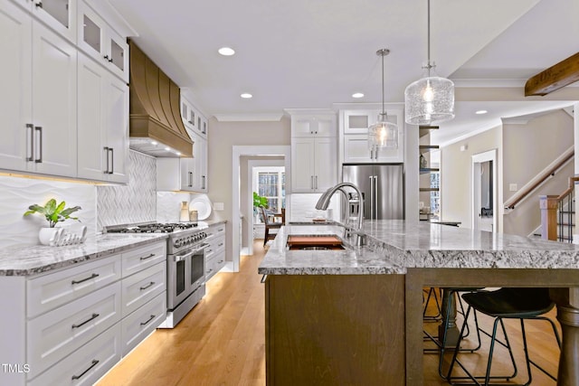 kitchen with hanging light fixtures, white cabinetry, stainless steel appliances, and a large island with sink