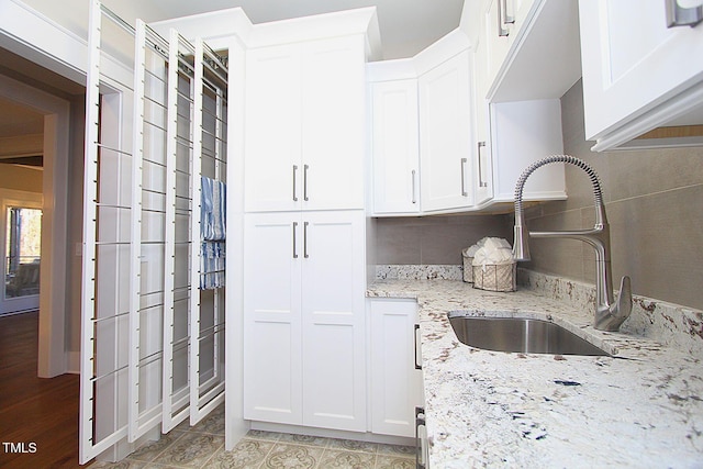 kitchen with light stone countertops, backsplash, white cabinetry, and sink