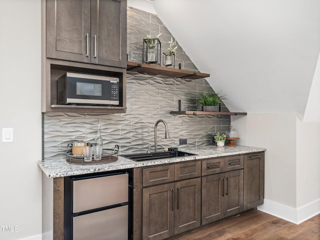 bar featuring light stone countertops, tasteful backsplash, vaulted ceiling, dark wood-type flooring, and sink