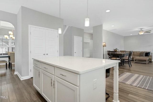 kitchen with ceiling fan with notable chandelier, a kitchen island, dark wood-type flooring, pendant lighting, and white cabinetry