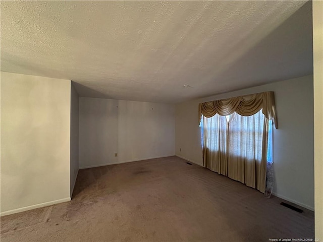 carpeted spare room with a textured ceiling, visible vents, and baseboards