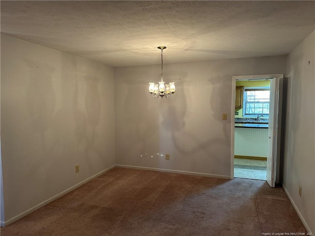 spare room featuring carpet, a textured ceiling, baseboards, and a notable chandelier