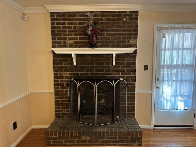 room details featuring a wainscoted wall, a brick fireplace, wood finished floors, and crown molding