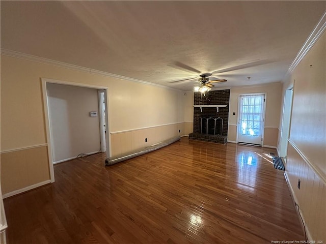 unfurnished living room featuring a fireplace, wood finished floors, a ceiling fan, wainscoting, and crown molding