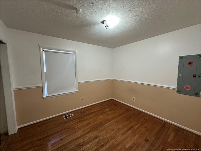 empty room with electric panel, baseboards, visible vents, wood finished floors, and a textured ceiling