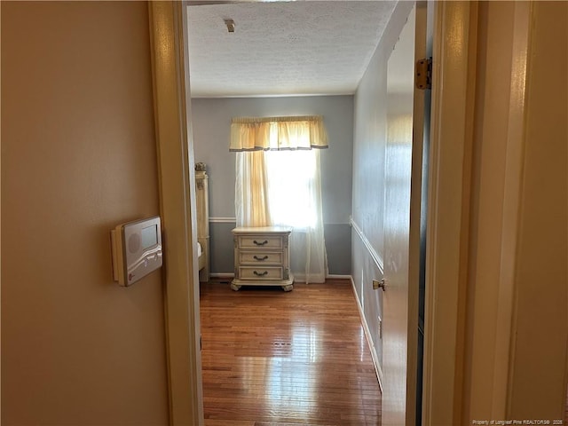 hall with a textured ceiling and wood finished floors