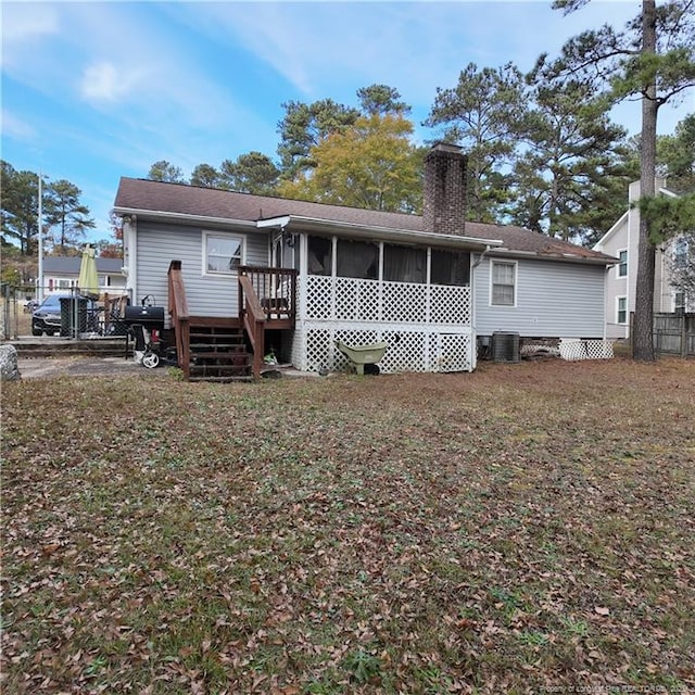 rear view of property with a chimney, a lawn, central AC unit, a sunroom, and fence