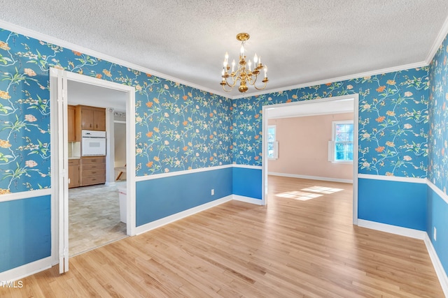 unfurnished room with an inviting chandelier, wood-type flooring, a textured ceiling, and ornamental molding