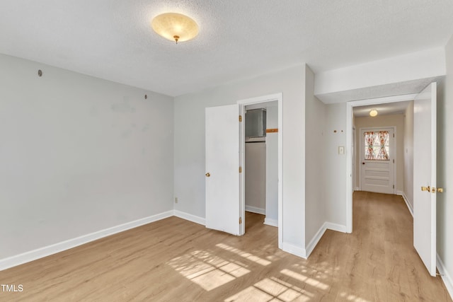 unfurnished bedroom featuring light hardwood / wood-style floors, a spacious closet, a textured ceiling, and a closet