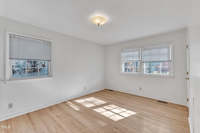 spare room with a textured ceiling and light hardwood / wood-style flooring