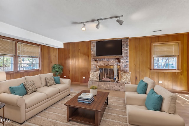 living room with a fireplace, a textured ceiling, rail lighting, and wood walls