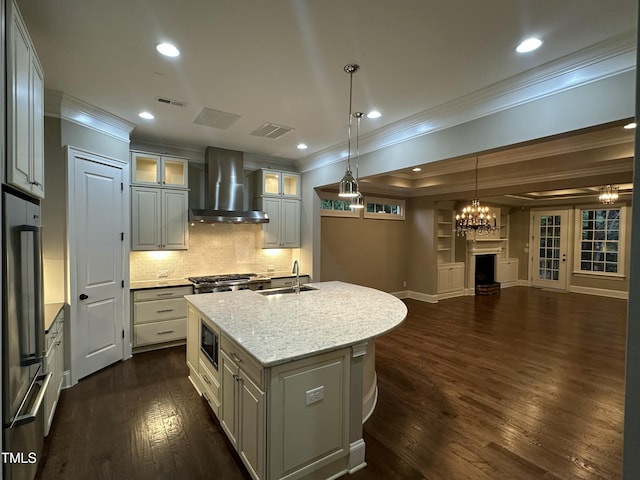 kitchen featuring light stone countertops, wall chimney range hood, dark hardwood / wood-style floors, crown molding, and a kitchen island with sink