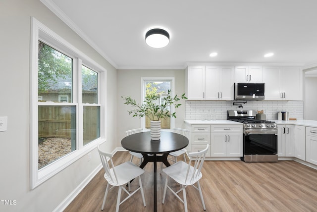 kitchen with appliances with stainless steel finishes, light wood-type flooring, white cabinetry, and ornamental molding