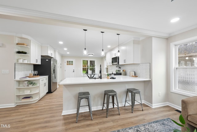 kitchen with kitchen peninsula, a kitchen bar, stainless steel appliances, pendant lighting, and white cabinetry