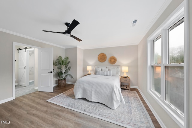 bedroom featuring ceiling fan, a barn door, wood-type flooring, and ornamental molding