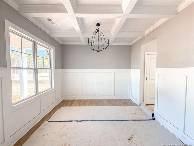 unfurnished dining area with coffered ceiling, beam ceiling, a chandelier, and light hardwood / wood-style floors