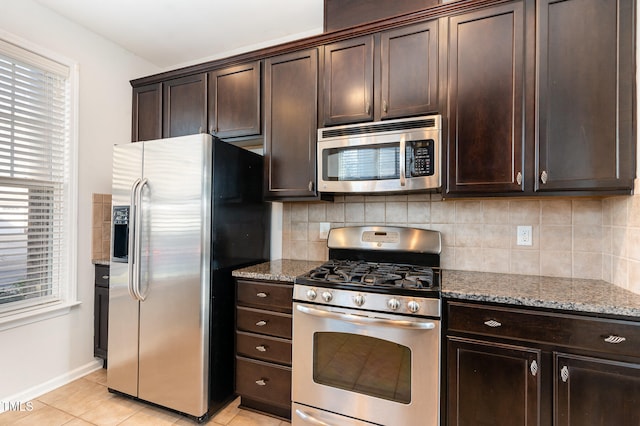 kitchen with decorative backsplash, dark brown cabinets, stainless steel appliances, light tile patterned floors, and stone counters