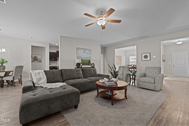 living room with ceiling fan with notable chandelier and light hardwood / wood-style floors