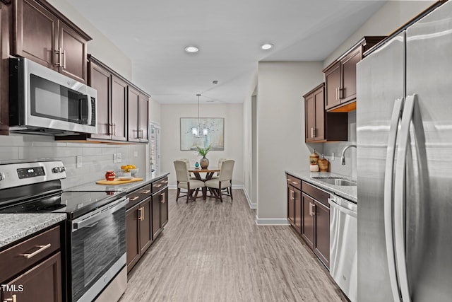 kitchen with light stone countertops, stainless steel appliances, sink, decorative light fixtures, and an inviting chandelier