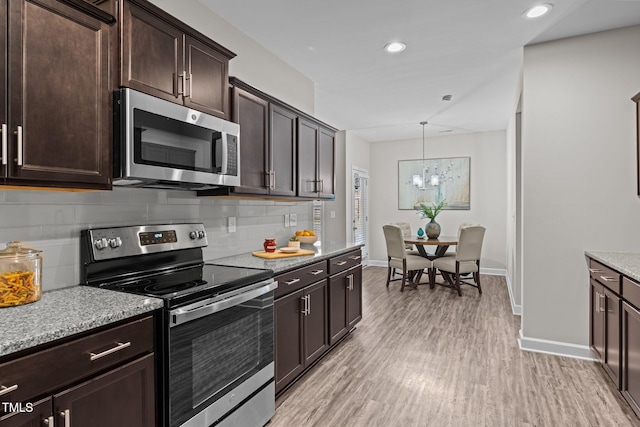 kitchen featuring tasteful backsplash, a chandelier, pendant lighting, appliances with stainless steel finishes, and light wood-type flooring