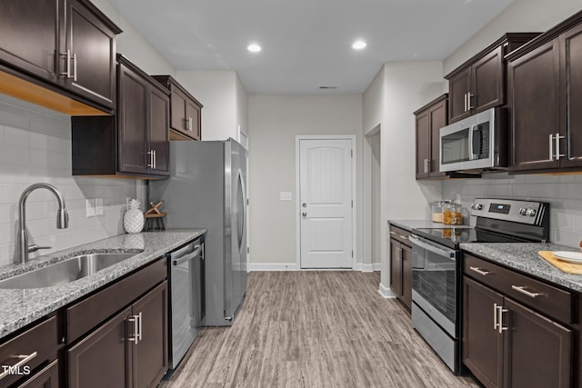 kitchen featuring light stone countertops, sink, stainless steel appliances, light hardwood / wood-style floors, and decorative backsplash