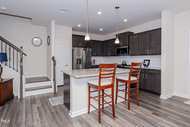 kitchen featuring light stone counters, light hardwood / wood-style floors, decorative light fixtures, a breakfast bar, and appliances with stainless steel finishes