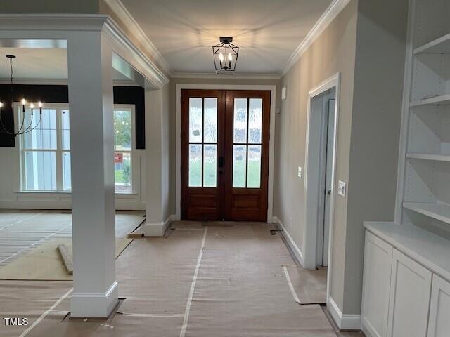 doorway to outside featuring french doors, crown molding, a notable chandelier, and a healthy amount of sunlight