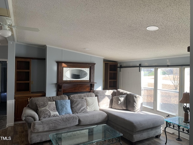 living room with ceiling fan, a barn door, crown molding, wood-type flooring, and a textured ceiling