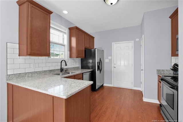 kitchen featuring kitchen peninsula, appliances with stainless steel finishes, light wood-type flooring, backsplash, and sink