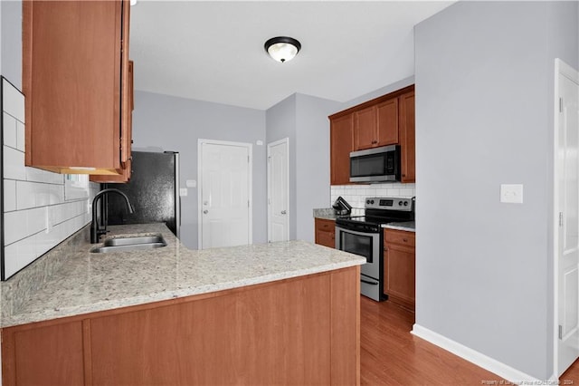 kitchen with kitchen peninsula, appliances with stainless steel finishes, tasteful backsplash, sink, and light hardwood / wood-style floors