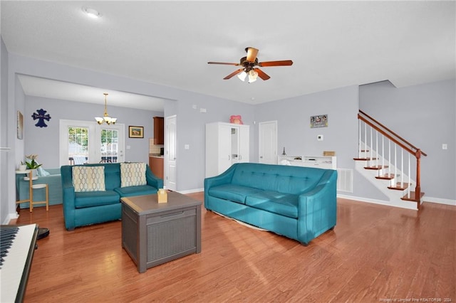 living room featuring ceiling fan with notable chandelier and light wood-type flooring