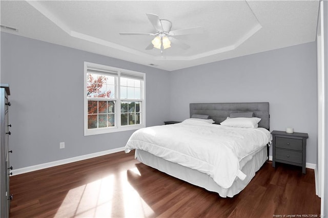 bedroom with ceiling fan, a raised ceiling, and dark wood-type flooring